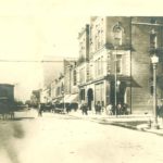 Photo of Main Avenue with horse-drawn carriages, cars and people. Around 1900.