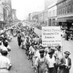 Protesters carrying a sign that says United Textile Workers of America, marching down Main Avenue 1929