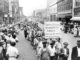 Protesters carrying a sign that says United Textile Workers of America, marching down Main Avenue 1929