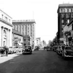 Cars parked along and driving on Main Avenue in 1938