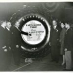 People standing around and pointing to a large Firestone "earth mover" tire
