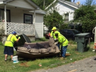 Crews in yellow vests lifting an old couch into a garbage truck