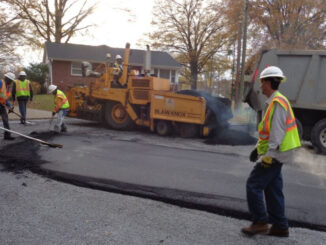 Six men using heavy equipment and tools to repave a street