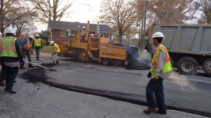 Six men using heavy equipment and tools to repave a street