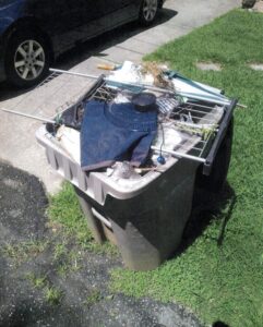 Recycling bin filled with trash including discarded clothing