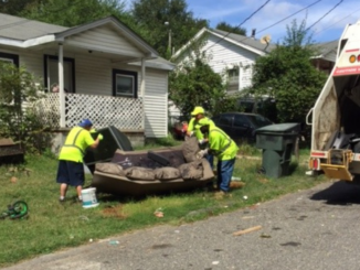 Three employees lift a discarded couch at the curb