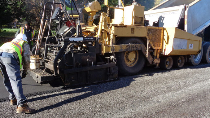 Big machine putting asphalt on street with employees assisting