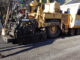 Big machine putting asphalt on street with employees assisting