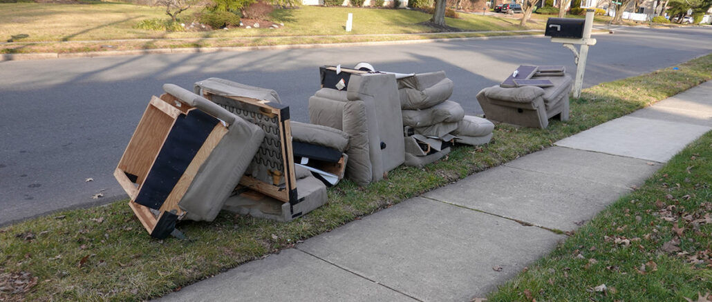 Parts of a sofa and chairs in grass next to a street