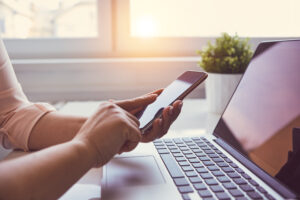 Woman using laptop texting on smartphone